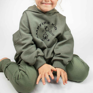 Child kneeling in forest green hooded sweatshirt with close-up of 'Campfire Kid' graphic, showcasing oversized fit by My Mini Explorer