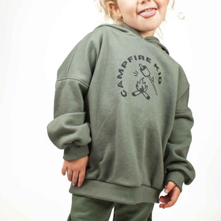 Child wearing forest green hooded sweatshirt with 'Campfire Kid' graphic, featuring oversized fit by My Mini Explorer. Handmade in Montana near Glacier National Park