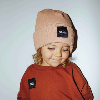 Rose clay colored beanie with a patch stating Mini Explorer. The little girl is also wearing a mini explorer patched signature crewneck. 