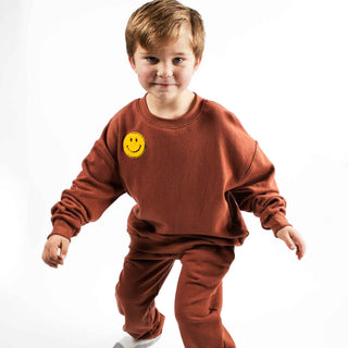 Tawny colored crewneck sweatshirt with an added smiley patch. Made with organic cotton in Montana USA